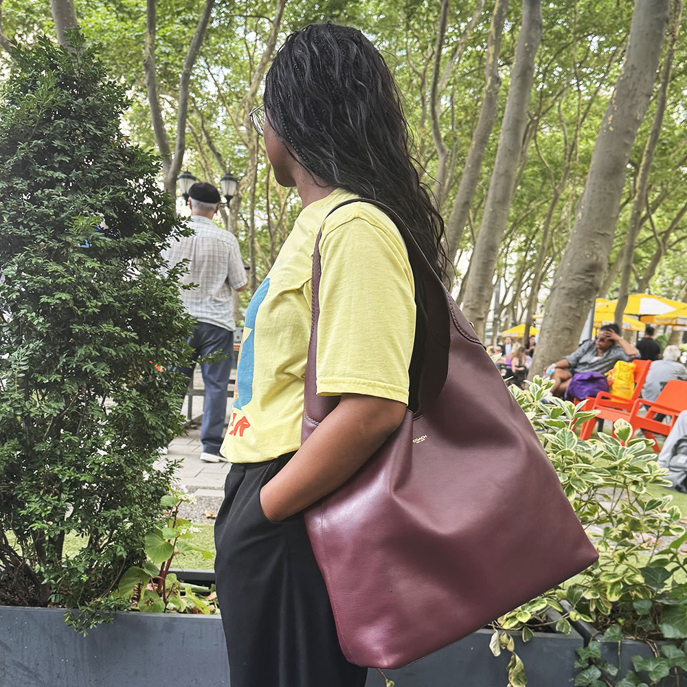 A woman in a yellow t-shirt, black pants, and a burgundy Coach Brooklyn Shoulder bag in NYC
