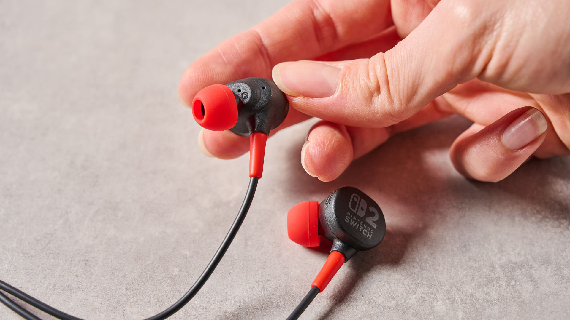 Person holding right bud of PowerA Wired Earbuds for Nintendo Switch 2