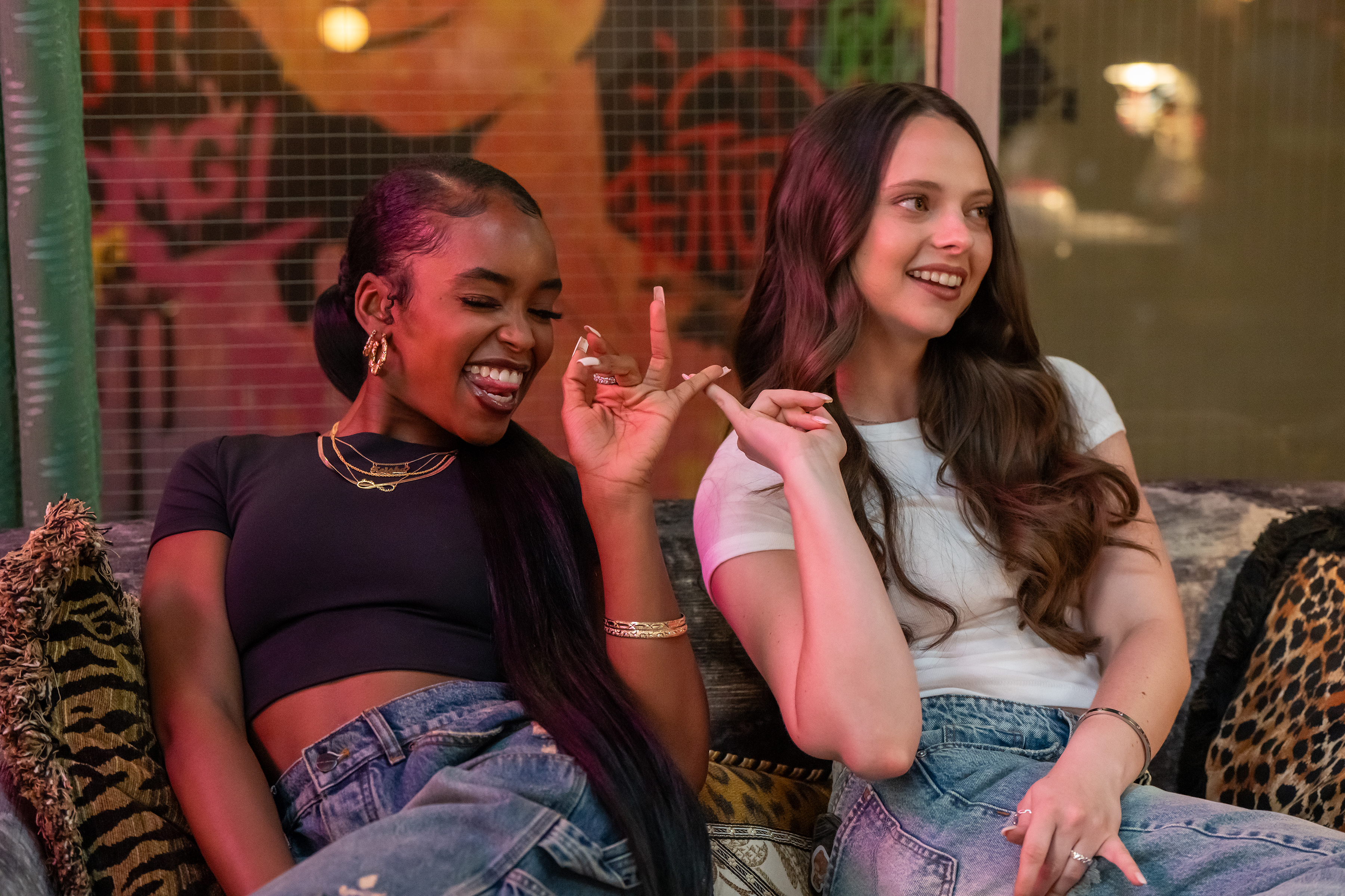 Ali Gallo as Chloe sitting with Lovie Simone as Keisha Clark touching their fingers together and smiling in the tv show forever
