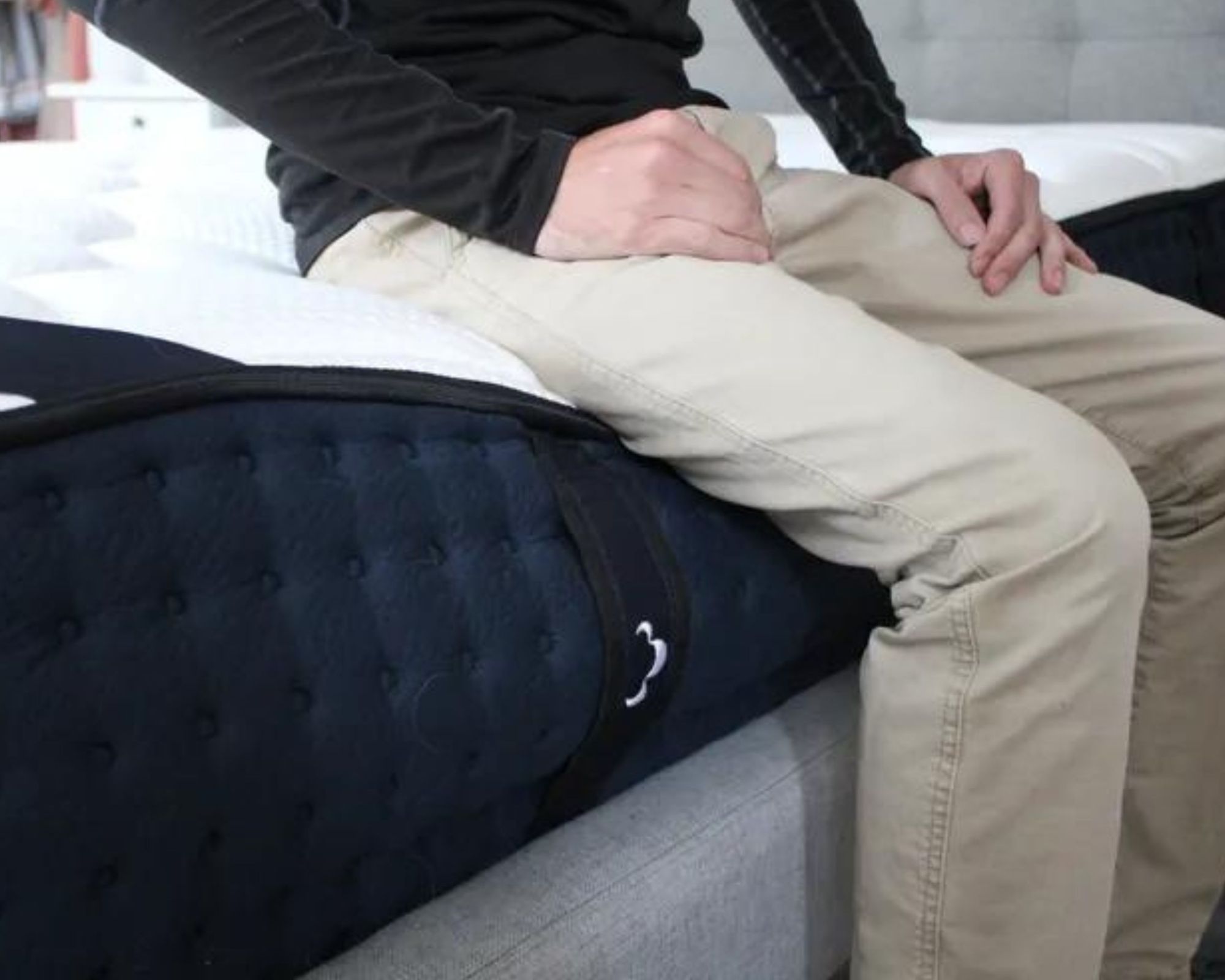 A person wearing pale beige chinos and a black long-sleeve top testing the edge support of the DreamCloud Luxe Hybrid Mattress