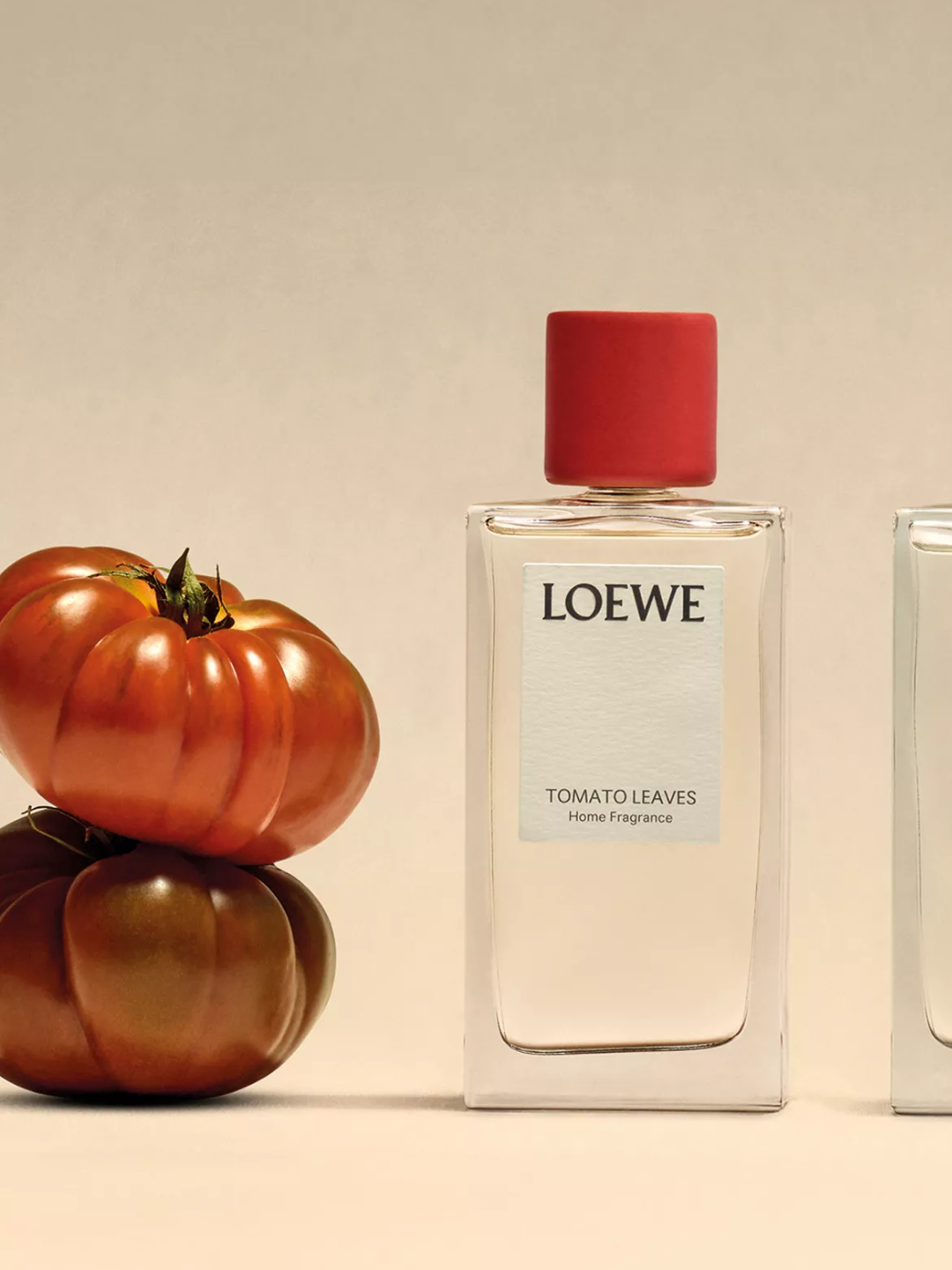 A glass bottle of room spray from Loewe beside a stack of heirloom tomatoes