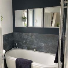Black walled with black marble tiles bathroom with a white bathtub and wall-mounted mirrors