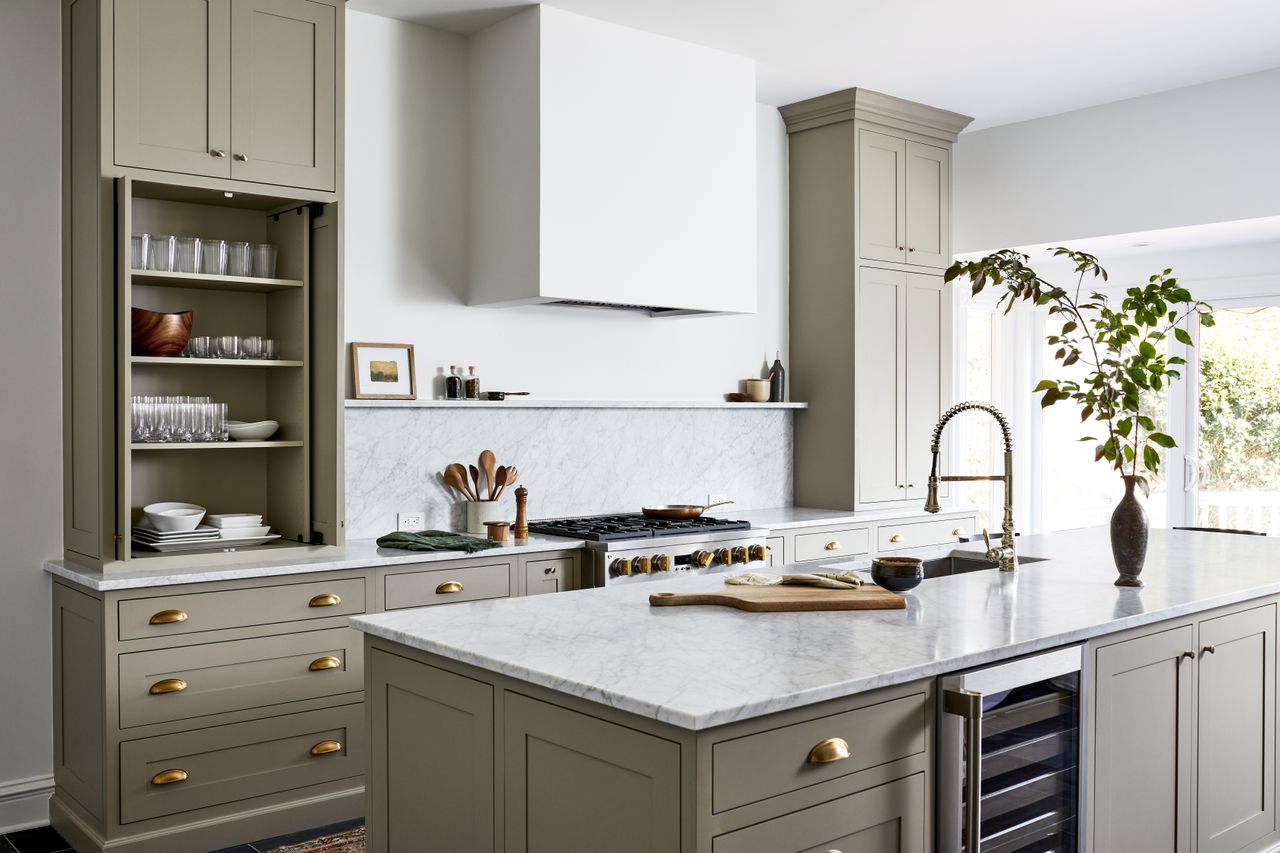 A sage green kitchen with door knobs and handles in brushed bronze