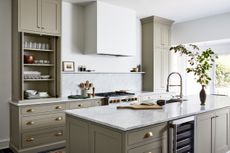 A sage green kitchen with door knobs and handles in brushed bronze