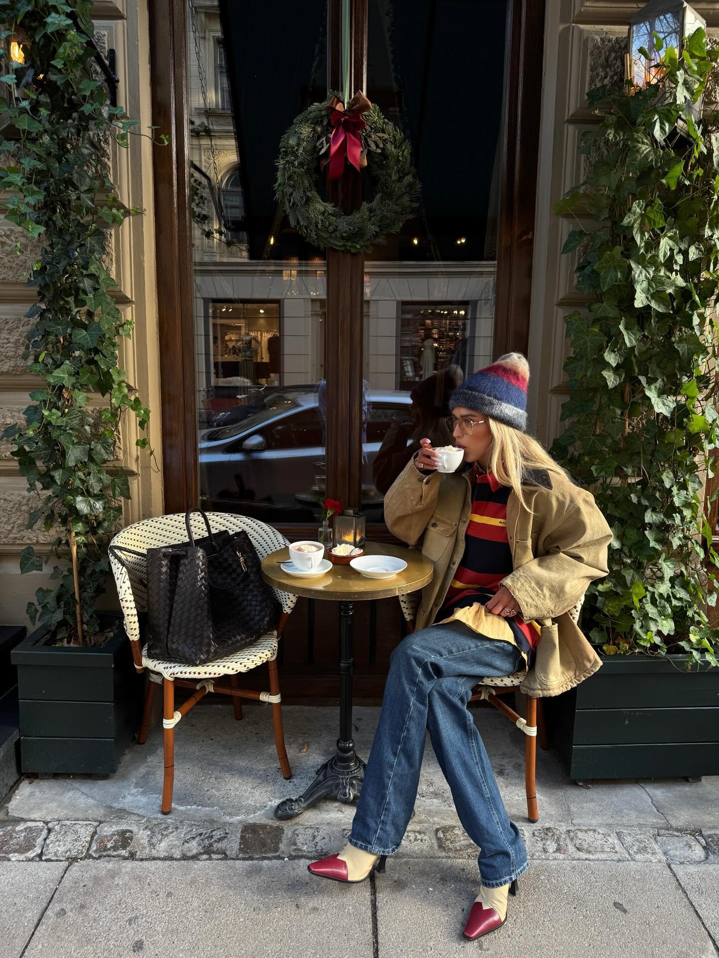 @emilisindlev wearing a tan jacket, striped sweater, cigarette jeans, and red-and-tan pointed-toe boots.