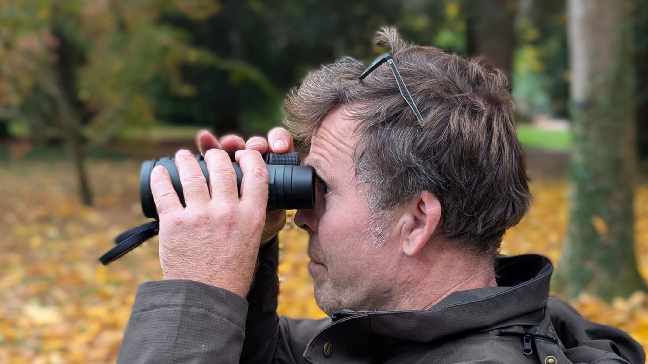 Our reviewer using the Carson VX 12x50 binoculars with autumn leaves on the ground behind him.
