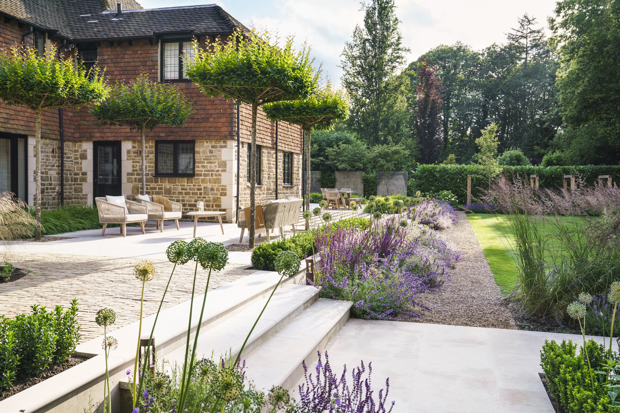 outdoor entertaining area in stepped garden with whimsical planting, a brick house, trees, and a seating area
