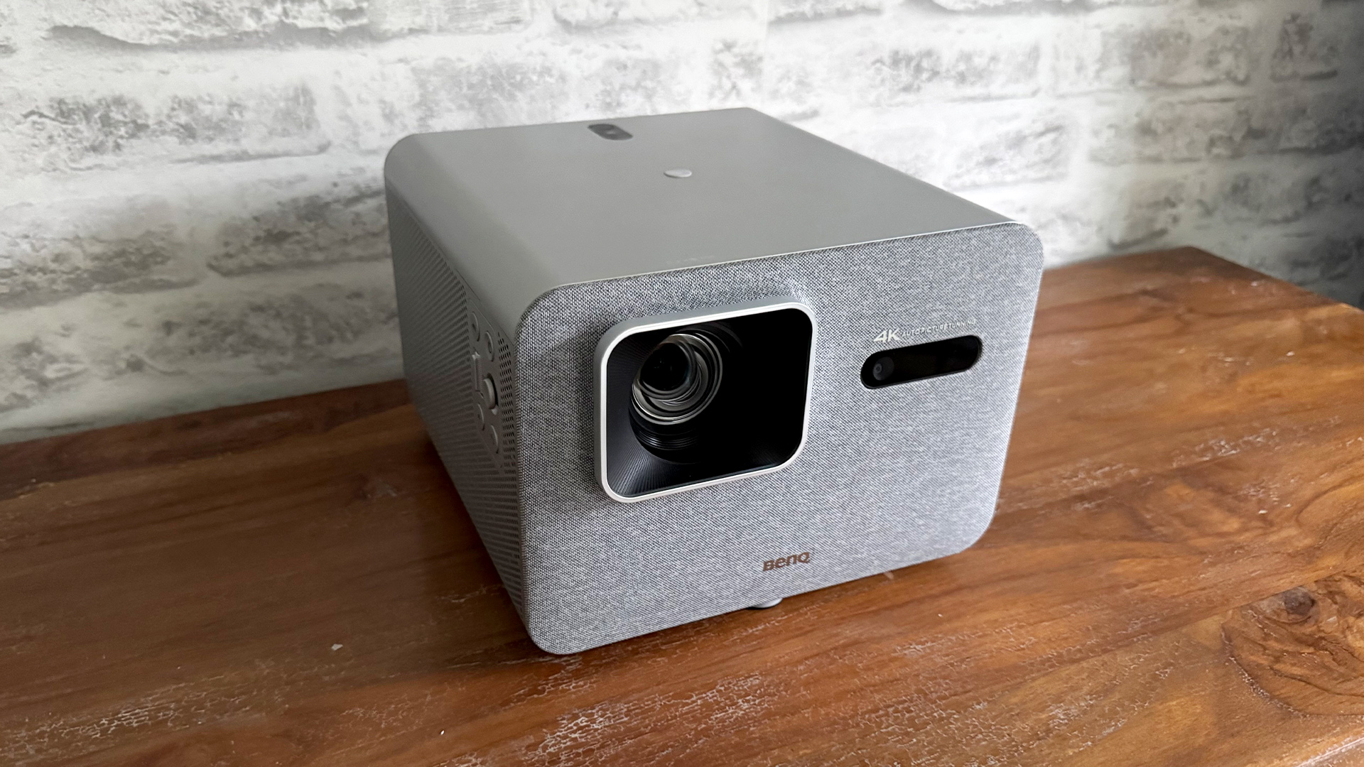 BenQ TK705i home cinema projector on wooden sideboard in front of white brick wall