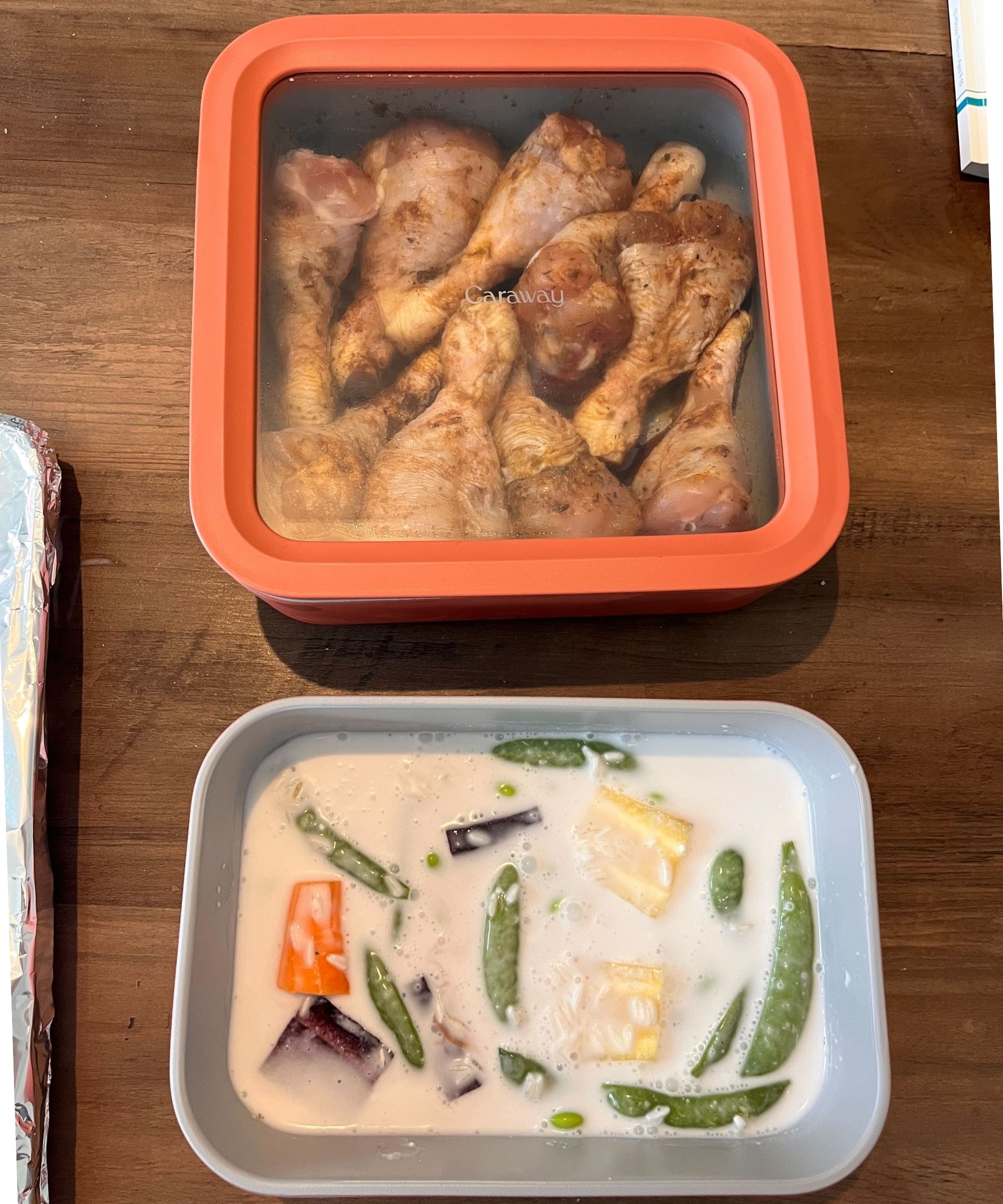 Caraway non toxic food container set showing two sizes. One has a coconut milk and vegetable rice mix ready for the oven. The other has marinated chicken drumsticks and a lid with glass for visibility