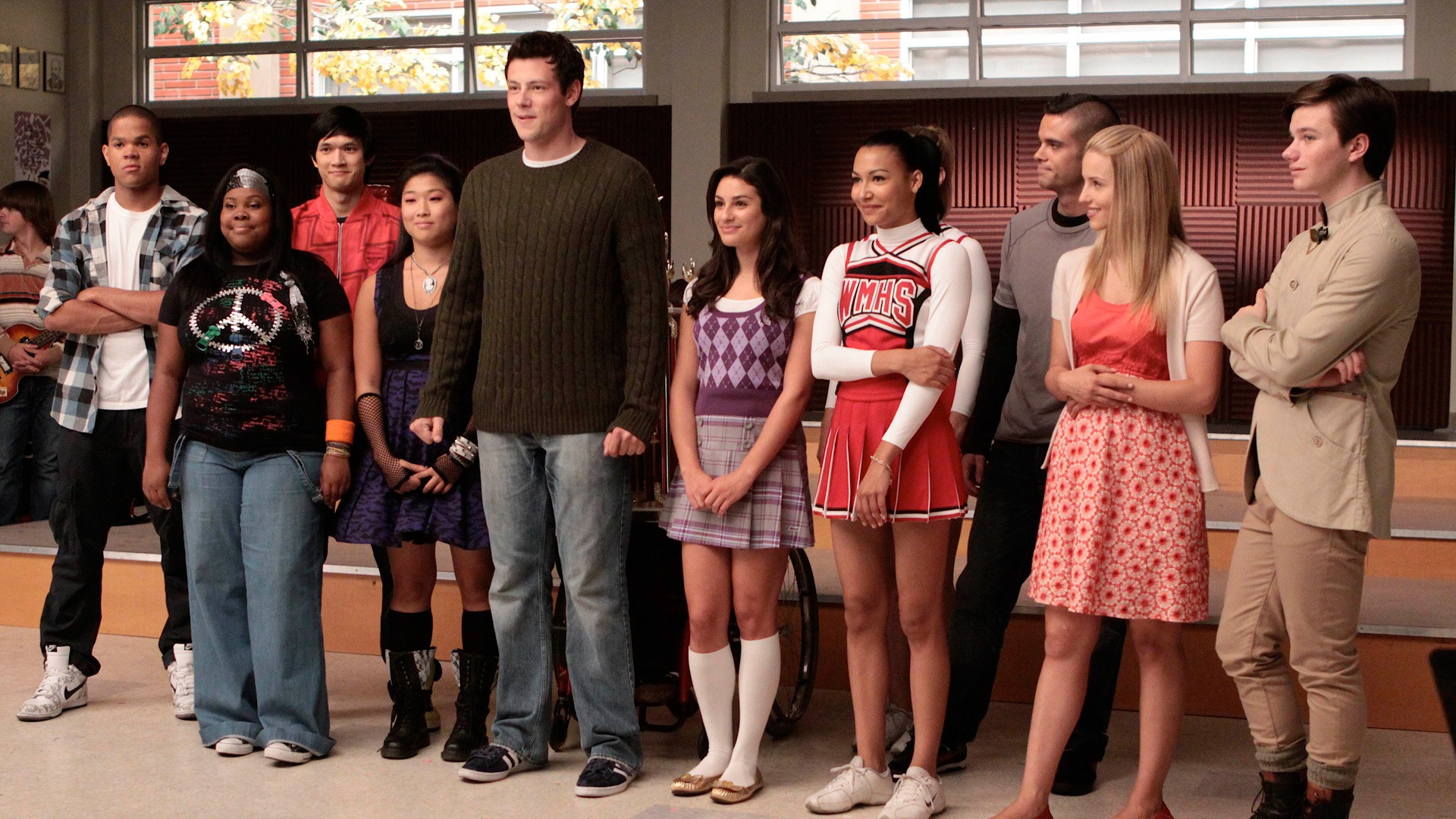 The cast of 'Glee' stands in a line in the choir room