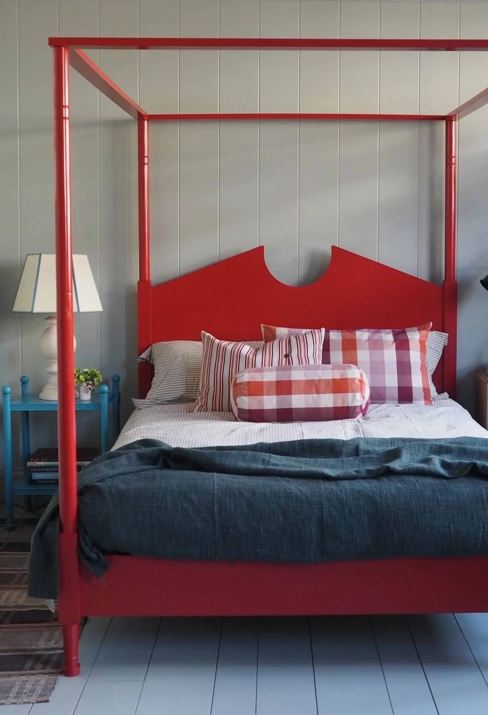 gray bedroom with wall paneling, red four poster bed, blue side table with lamp