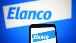 A phone bearing the Elanco logo on a blue background. Behind it, the Elanco logo is visible on a white background. Decorative: The Elanco logo is the word "Elanco" in a print font.