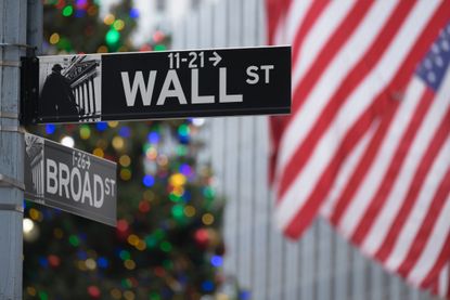 closeup of Wall Street and Broad Street signs in NYC with American flag and Christmas tree in background
