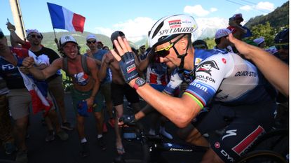Julian Alaphilippe waving and smiling as he rides through a crowd of cycling fans