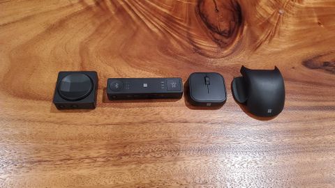 The D-pad, hub, mouse, and mouse tail/thumb rest for the Microsoft Accessible Accessories on a wooden surface