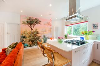 A pink kitchen with a large mural of a tree on one wall and a pink kitchen island