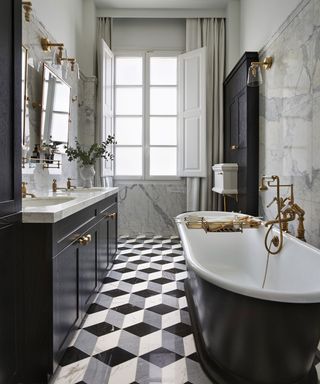 A black and white bathroom with a geometric tiled floor and a black roll top bath