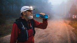 A man on a trail run stopping to take a drink of water from one of his bottles.