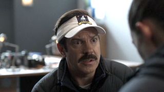 Ted wearing a visor looking concerned speaking to Alice in the locker room.