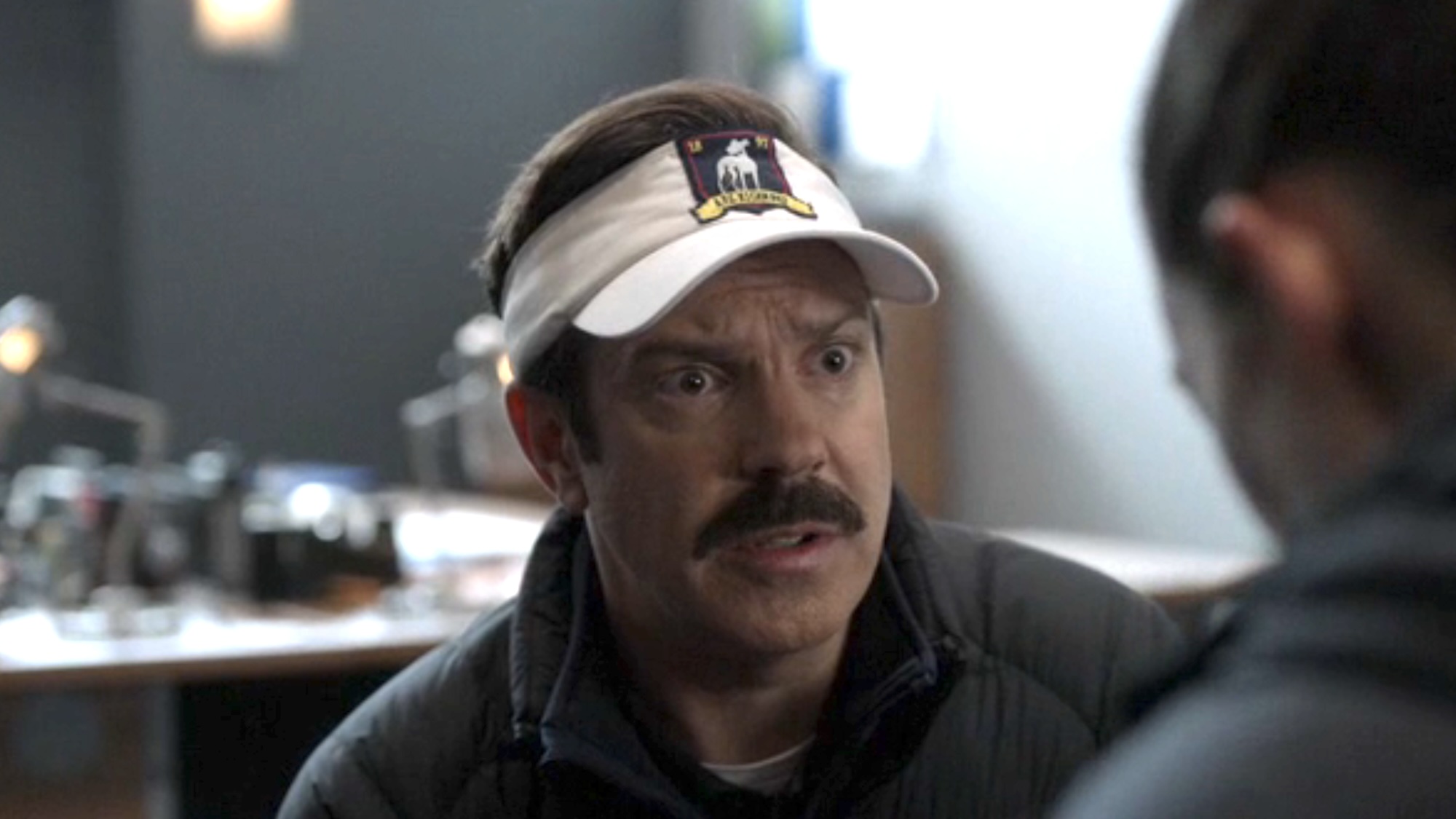 Ted wearing a visor looking concerned speaking to Alice in the locker room.