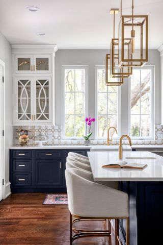 Painted kitchen cabinet ideas featuring midnight blue painted cabinetry, white countertops, dark wooden flooring and a kitchen island with upholstered seating.