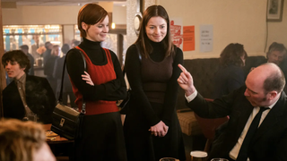 Dolours (Lola Petticrew) and Marian Price (Hazel Doupe) stand side-by-side in conversation with a man in a pub in Say Nothing