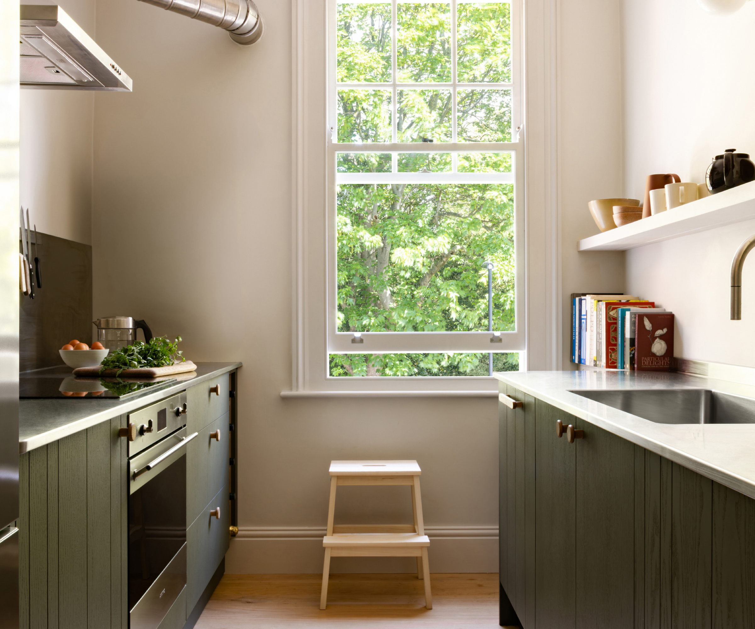 galley kitchen with green cabinets, window at end and open shelving above sink