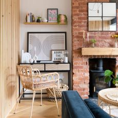 Living room with wooden panelling on the side, a brick fireplace with log burner, and a desk area with rattan desk chair