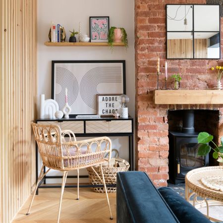 Living room with wooden panelling on the side, a brick fireplace with log burner, and a desk area with rattan desk chair