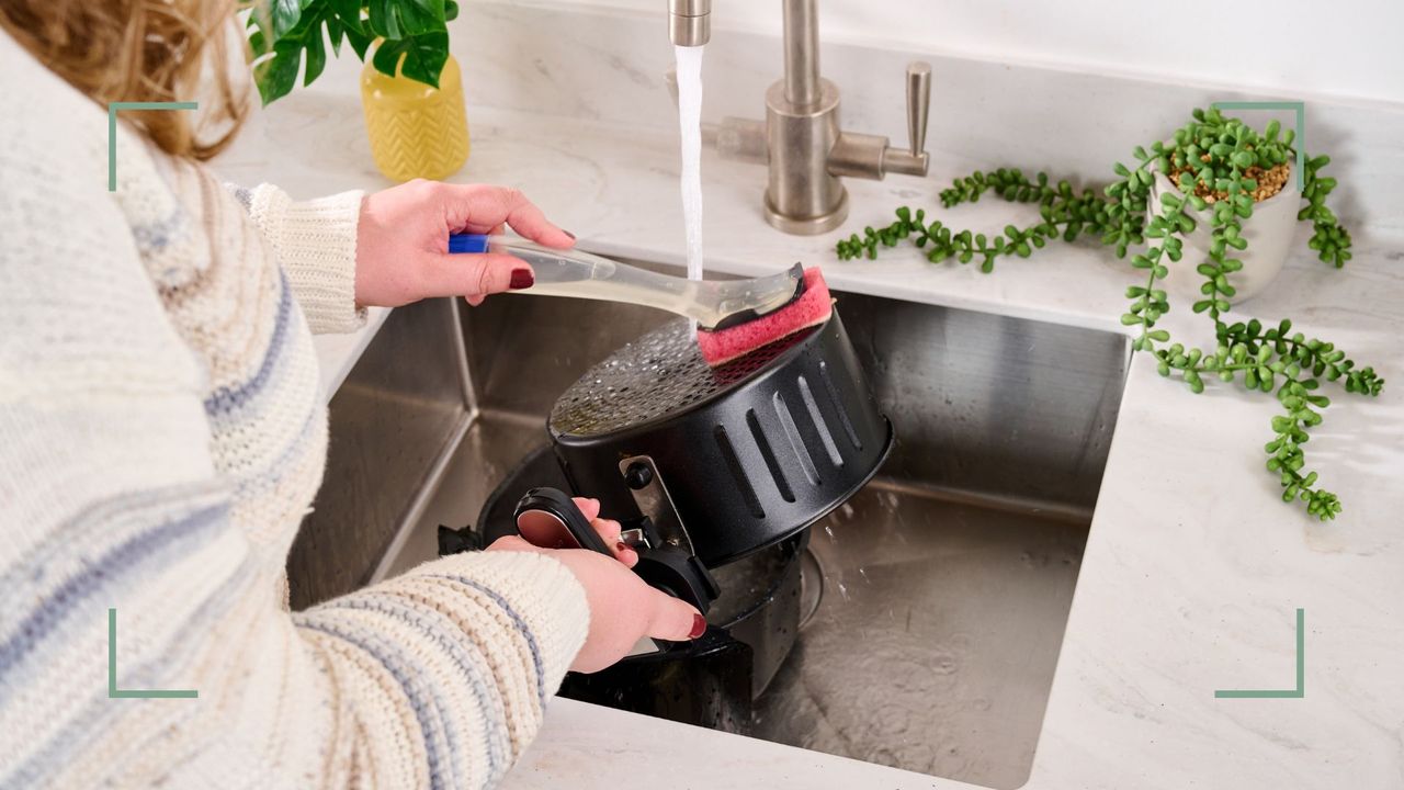 Person washing an air fryer by hand at a kitchen sink to show how to clean an air fryer