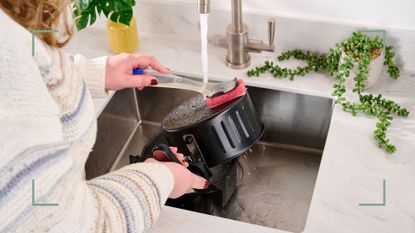 Person washing an air fryer by hand at a kitchen sink to show how to clean an air fryer