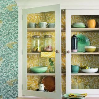 A kitchen cabinet as part of a pattern drenched scheme. Blue wallpaper beside it with yellow patterned wallpaper lining the interior