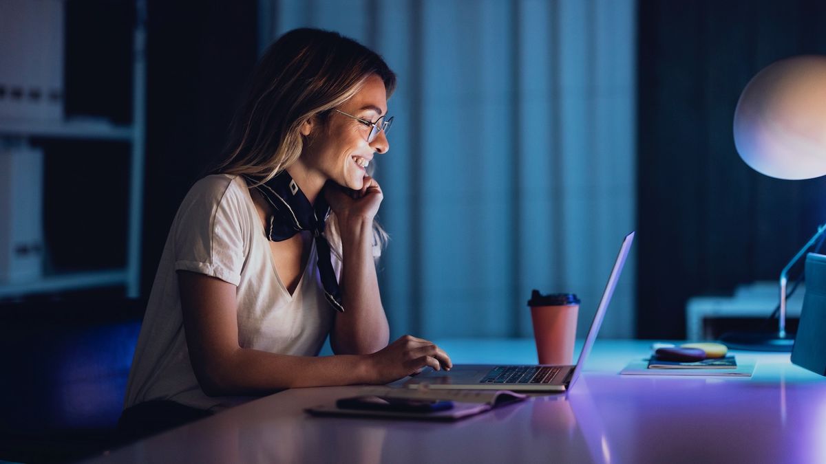 Person looking happy while using a laptop inside at night