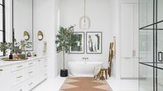 White bathroom with white countertop, white freestanding bath, potted tree, terracotta rug and brass wall sconce and ceiling pendant