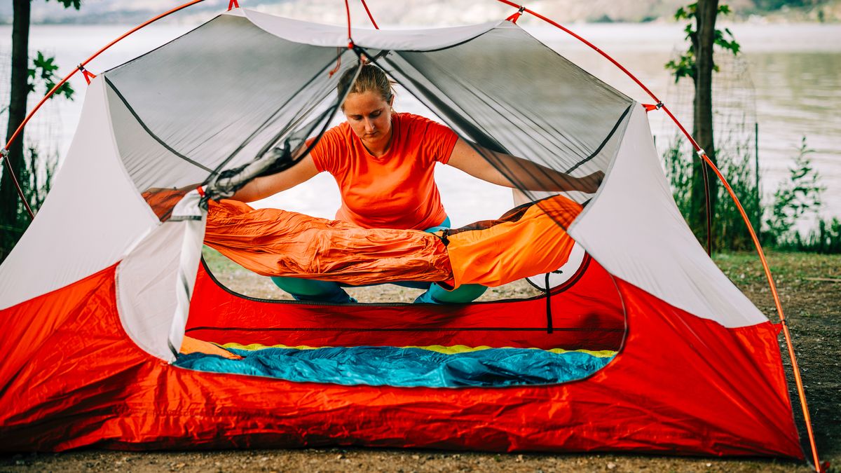 A woman lays out a sleeping bag inside a tent at a campground – she’ll want a sleeping bag liner too