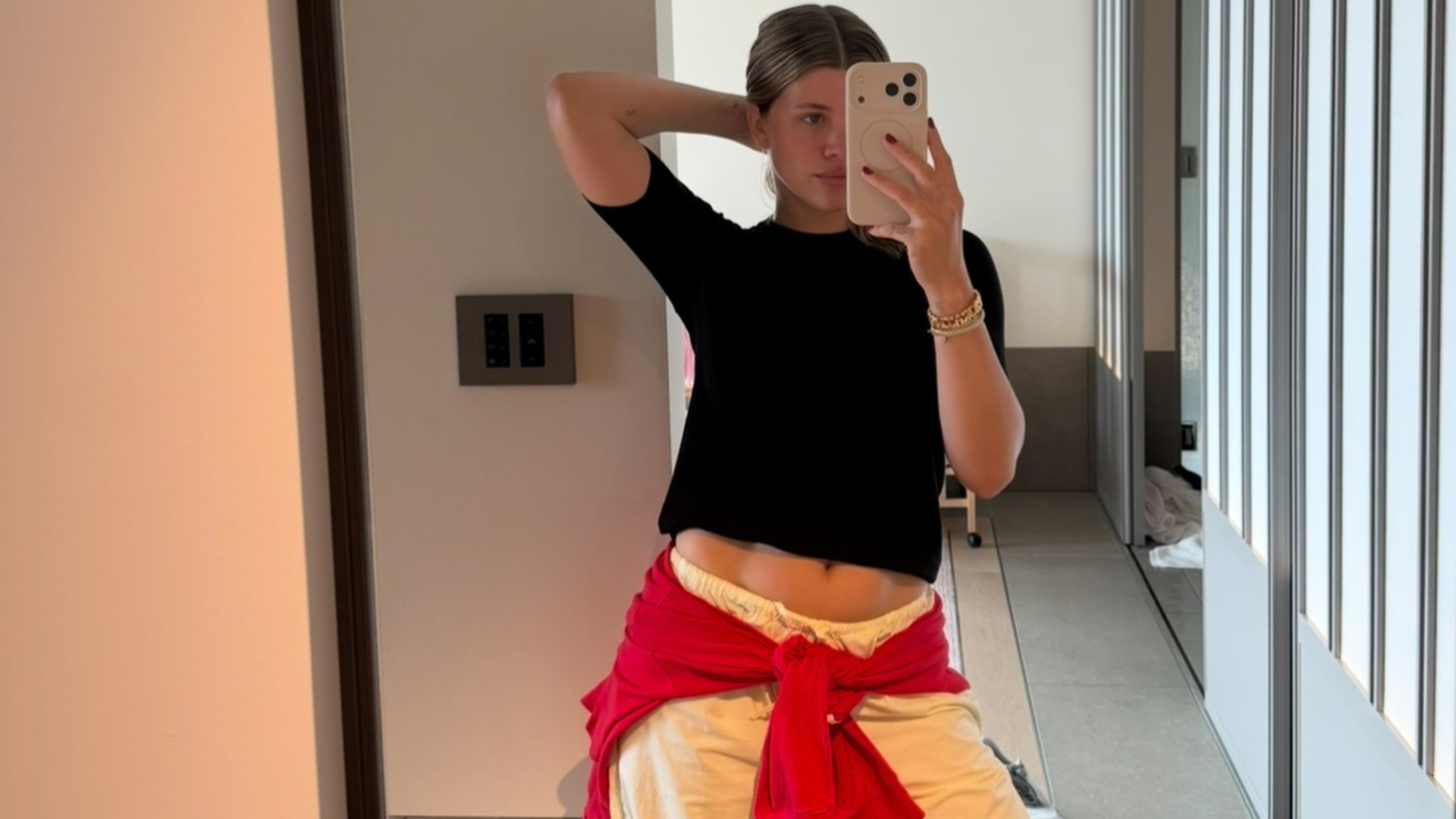 Sofia Richie wears a black tee, white pants, and a red sweater.