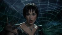 JLo wearing all black in front of a web singing the title song of 'Kiss of the Spider Woman'