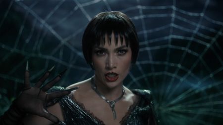 JLo wearing all black in front of a web singing the title song of 'Kiss of the Spider Woman'