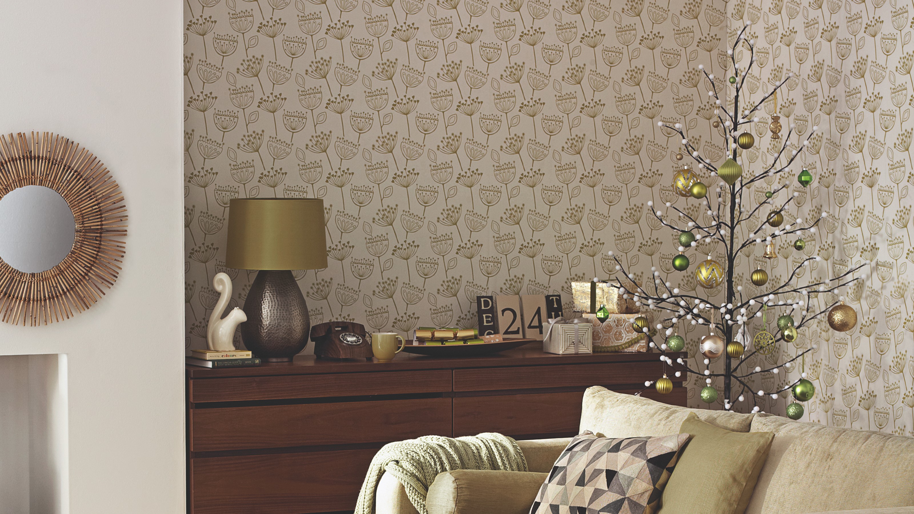 A living room with a botanical wallpaper with a twig Christmas tree in the corner decorated with green baubles