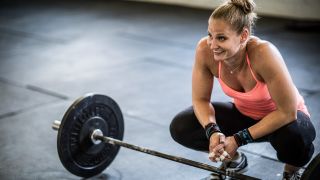 A woman crouches by a barbell