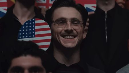 Timothee Chalamet smiling holding a table tennis paddle with an American flag on it in Marty Supreme