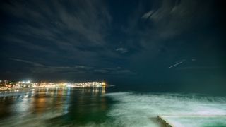 a meteor streaks overhead above a beach at night