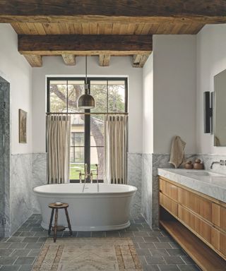 bathroom with stone floor and marble surround andw ooden vanity and freestandind porcelain tub