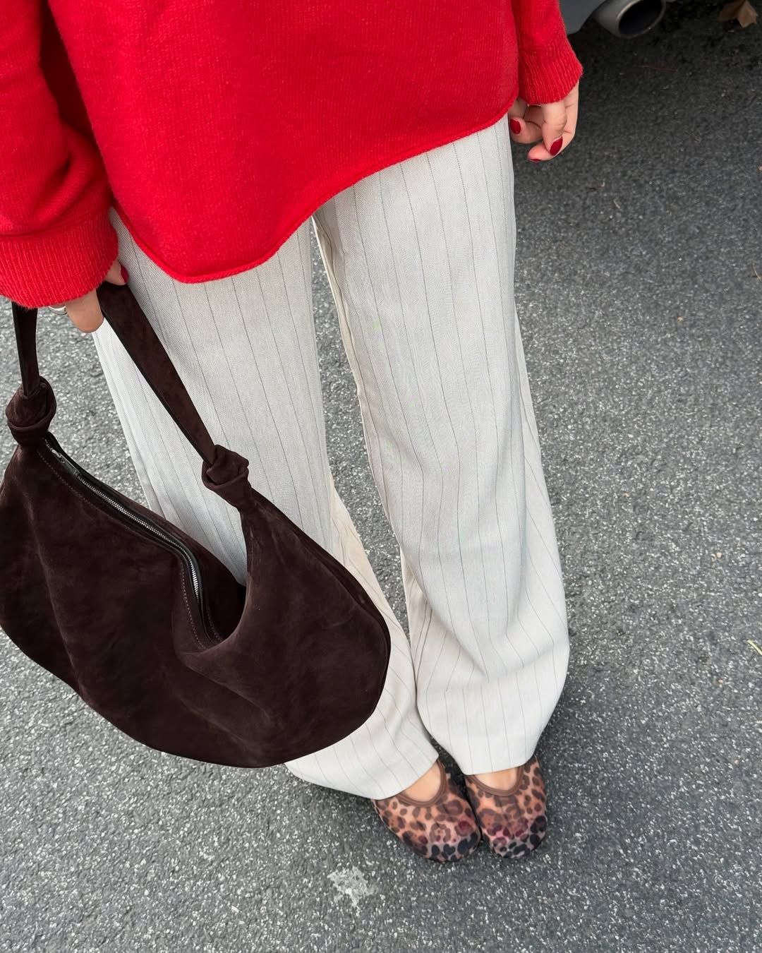 Woman in white pants, red sweater, brown bag, and leopard print ballet flats