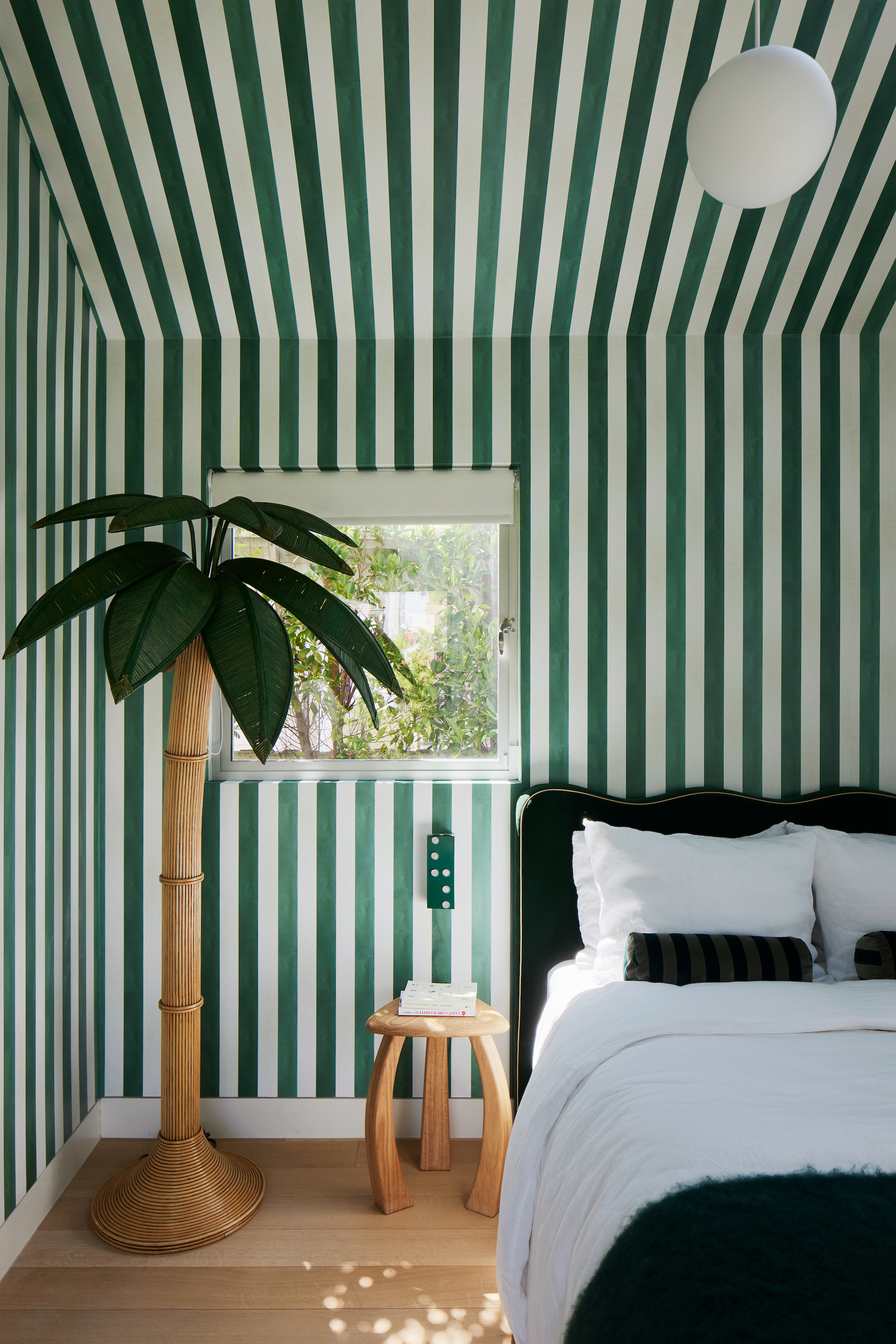 An emerald green and white striped walls with a small box window to the left corner and a white pendant light above the bed.