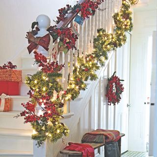 White staircase decorated with red and green garlands and fairy lights and wreath attached to staircase