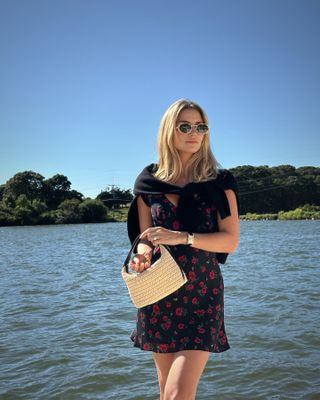 Woman wearing a short dress and Bottega Veneta sunglasses by the water.