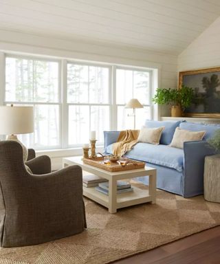 coastal living room with a pale blue slip covered linen sofa and a large woven rug with a green linen armchair