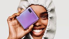 Samsung Galaxy Z Flip Android foldable phone held by a woman in a hoodie in front of her right eye while smiling