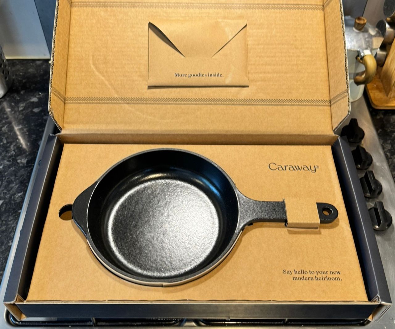 A black cast iron Caraway skillet in cardboard packaging.